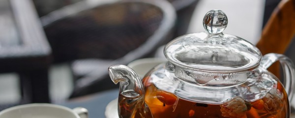 Hot cented tea with goji (chinese wolfberries) in transparent glass teapot and porcelain cup on black table
