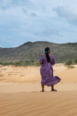 A Way&uacute;u woman back view in traditional outfit in sand dunes in the desert. La Macuira, La Guajira, Colombia