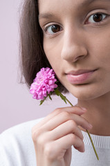 Portrait of a brown-Eyed girl on a pink background, holding a flower of lilac chrysanthemum