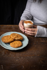 Woman sitting a table holding a coffee cup with a plate of biscuits in front of her