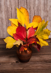 Autumn composition. Bouquet of colorful autumn leaves in a clay vase on a wooden background.