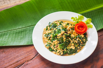  Green vegetables that are stir fried with eggs in a white dish placed on a wooden table.