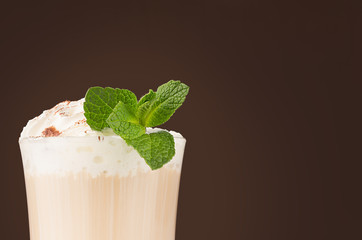 Refreshment coffee drink with fresh green mint, whipped cream, chocolate powder closeup, details, top sections of glass on dark brown background.