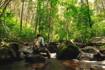 Man sitting on rock in rainforest with backpack among Small streams flow through abundant tropical forest concept summer vacations outside alone into the wild of Thailand,Phang Nga,Koh Yao Yai