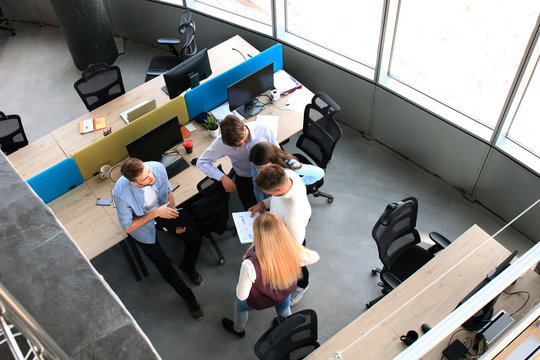 Top view of young modern colleagues in smart casual wear working together while spending time in the office.