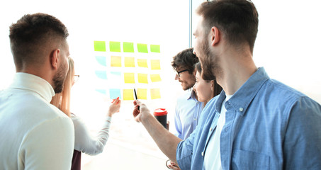 young creative startup business people on meeting at modern office making plans projects with post stickers on glass.