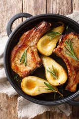 Tasty hot pork chops baked with pears and rosemary in honey sauce in a pan close-up. Vertical top view