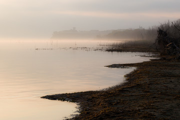 Beautiful view of Trasimeno lake (Umbria) shore at dawn, with Castiglione del Lago town at the distance