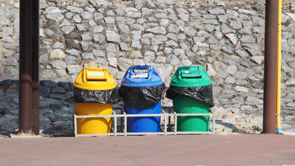 Obraz premium Three bin yellow blue and green in the park.Have stone wall in the background.