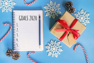 2020 New year concept. Goals 2020 list in notepad, gift box and christmas decoration on blue pastel color with copy space