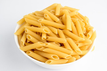 Dried penne Italian pasta in a round bowl ready to be cooked, isolated on white table, with view from above 