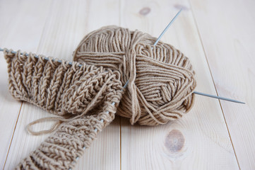a skein beige of woolen red thread, with knitting needles for hand knitting on a wooden table