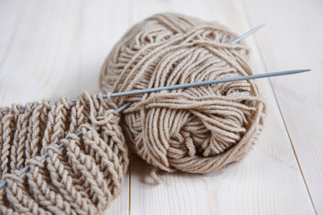 a skein beige of woolen red thread, with knitting needles for hand knitting on a wooden table