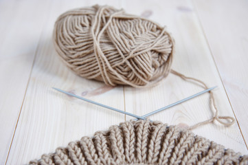 a skein beige of woolen red thread, with knitting needles for hand knitting on a wooden table