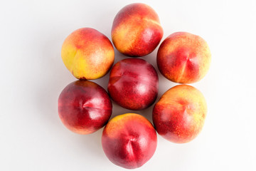 Seven fresh ripe nectarine fruits displated as a flower on a white table, isolated on white, with soft focus, top view