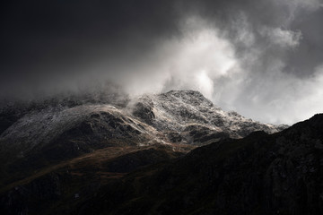 Stunning moody dramatic Winter landscape image of snowcapped Tryfan mountain in Snowdonia with stormy weather brooding overhead