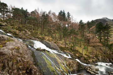 Stunning landscape image of Ogwen Valley river and waterfalls during Winter with snowcapped mountains in background
