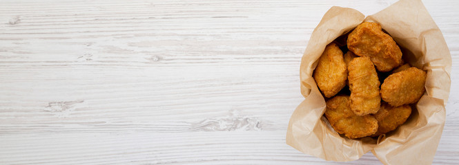 Chicken nuggets in a paper box over white wooden surface. Overhead, from above, flat lay. Space for text.