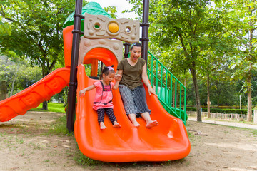 Mom and daughter  playing on play ground play slider seesaw,  Funny Asian family in a park