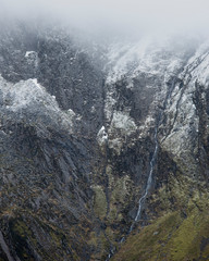 Stunning dramatic landscape image of snowcapped Glyders mountain range in Snowdonia during Winter with menacing low clouds hanging at the peaks