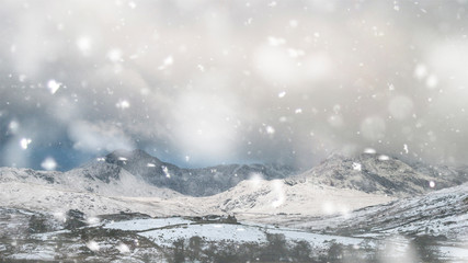 Beautiful Winter landscape image of Llynnau Mymbyr in Snowdonia National Park with snow capped mountains in background in heavy snow storm