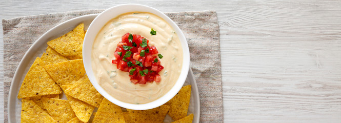 Homemade cheesy dip in a bowl, yellow tortilla chips, top view. Flat lay, overhead, from above. Space for text.