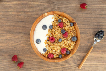 Breakfast smoothie bowl with granola, fresh raspberries, blueberries and yogurt on wooden background.