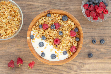 Breakfast smoothie bowl with granola, fresh raspberries, blueberries and yogurt on wooden background.