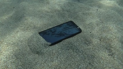Smartphone lies on a cave seabed on its screen reflects the surface of blue water with small waves. Underwater view. Mediterranean Sea, Europe.