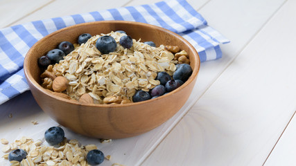 wooden bowl with oatmeal and blueberries on a white table next to a blue napkin