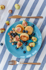 Fresh cheese pancake, ripe figs, jujube, blueberry and raw hazelnuts on a blue plate.