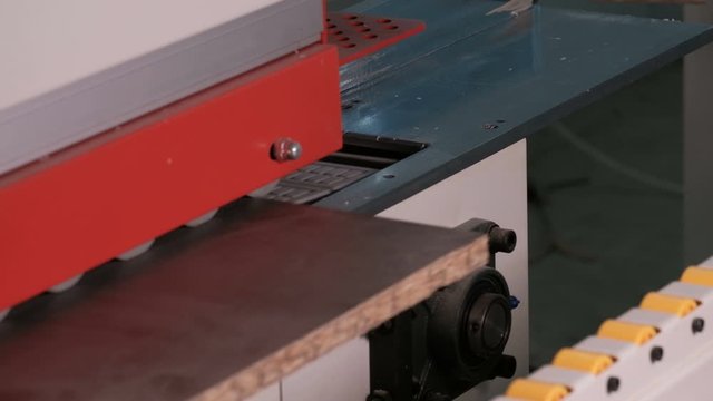 Machine for gluing edges on chipboard parts. Furniture manufacture. Shallow depth of field, selective focus. The mechanism of automatic movement of the rollers on the machine.