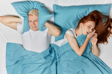 ginger woman snoring in sleep and blonde man suffering on a bed. top view photo. close up photo.