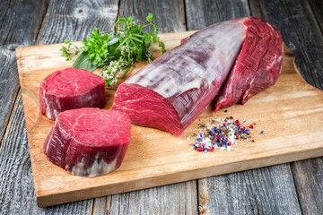 Rohes dry aged Rinderfilet Medaillon Steak natur als closeup mit Gewürzen und Salz angeboten auf einem Holz Schneidebrett