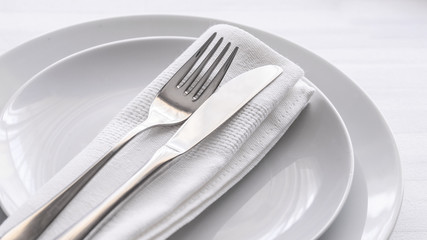 Close up of silverware fork and knife with napkin on white porcelaine plate. Copy space. Restaurant...