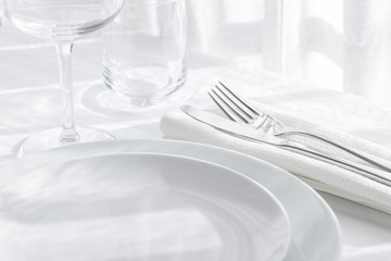 Table setting white and grey colour. Empty glasses and plates set with napkin and cutlery on white table cloth. Restaurant interior background.