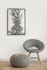Comfortable chair and pouf near light wall with picture