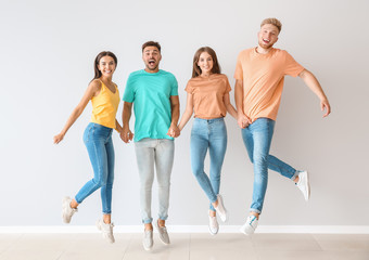 Naklejka premium Group of jumping young people in stylish casual clothes near light wall