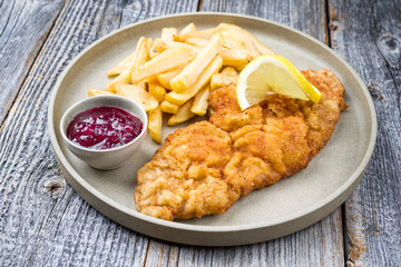 Frittiertes Wiener Schnitzel vom Kalb von der Oberschale mit Pommes Fritesmit Preiselbeeren Marmelade als closeup auf einem Modern Design Teller