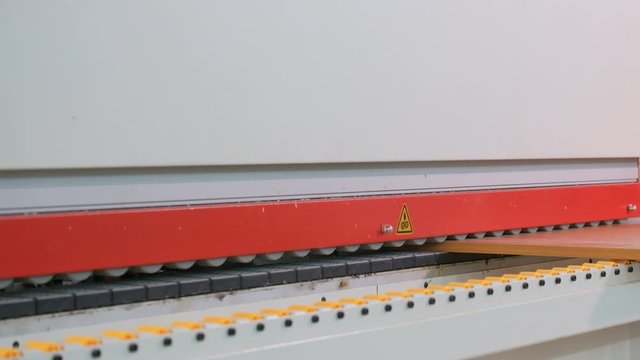 Machine for gluing edges on chipboard parts. Furniture manufacture. Shallow depth of field, selective focus. The mechanism of automatic movement of the rollers on the machine.