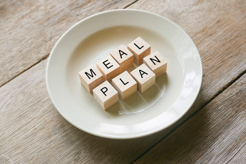 Wooden cube written with 'MEAL PLAN' on plate on wooden background. Food and diet concept.
