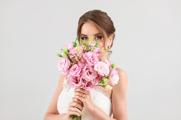 Portrait of beautiful young bride with wedding bouquet on light background