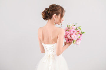 Beautiful young bride with wedding bouquet on light background, back view