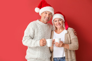 Portrait of happy mature couple in Christmas hats and with cups of hot cacao on color background