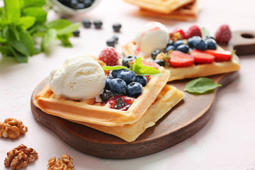 Board with tasty waffles, ice-cream and berries on table