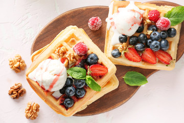Board with tasty waffles, ice-cream and berries on table