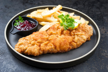 Deep fried Wiener schnitzel from veal topside with French fries and cranberry sauce as closeup...