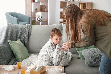 Mother giving medicine to her son ill with flu at home