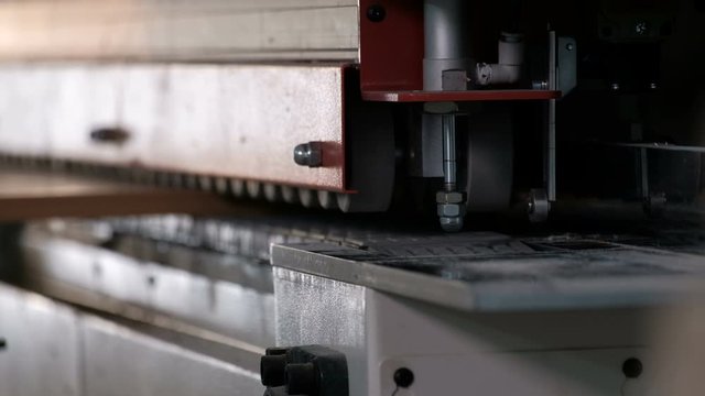 Machine for gluing edges on chipboard parts. Furniture manufacture. Shallow depth of field, selective focus. The mechanism of automatic movement of the rollers on the machine.