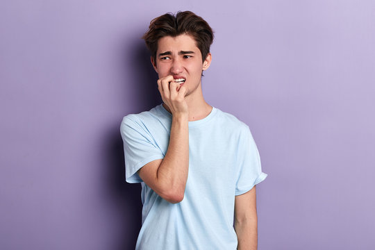 puzzled nervous man biting his nails , expressing negative feeling and emotion isolated on blue background with copy space, close up portrait
